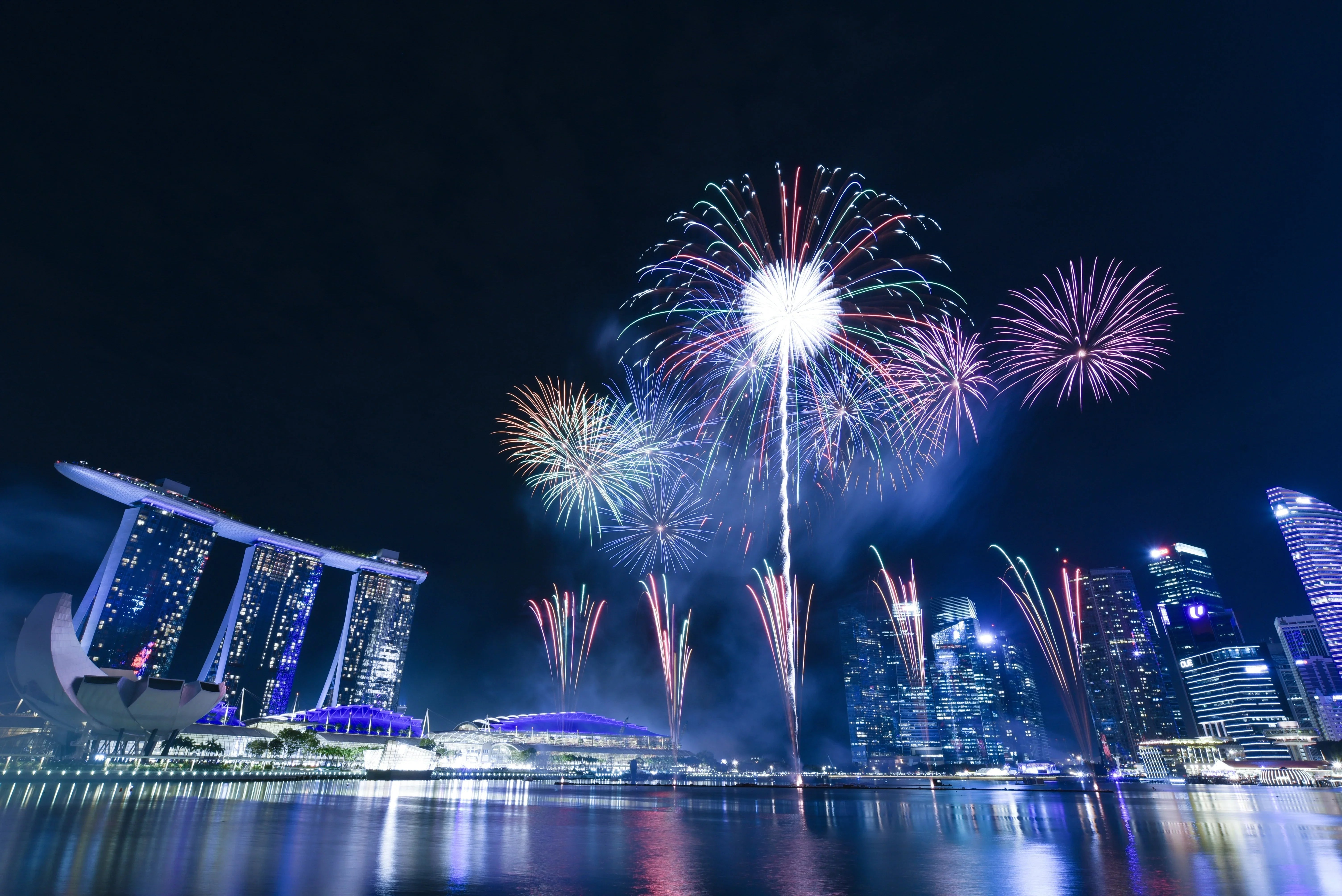 Colorful fireworks over a modern city skyline at night reflecting on water