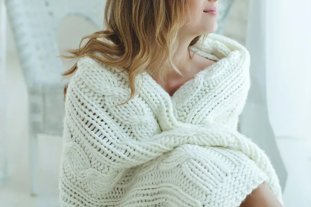 Woman wrapped in a chunky knit white organic cotton blanket in a bright room