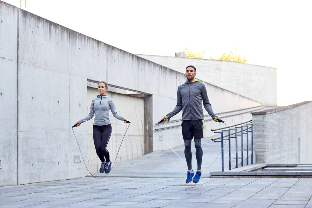 Man and woman in activewear jumping rope outdoors on concrete urban steps