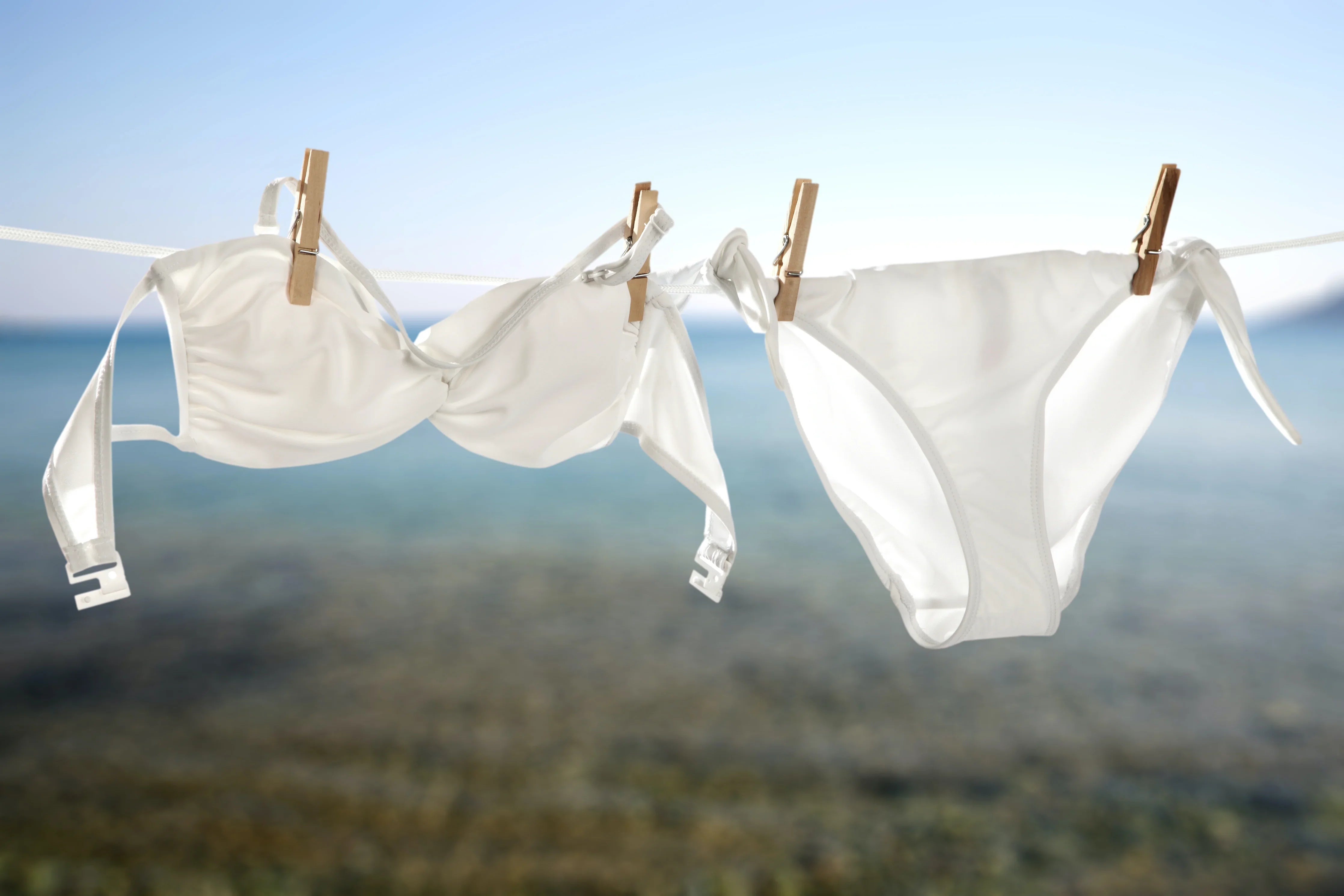 White bra and panties hanging on clothesline outdoors with ocean background