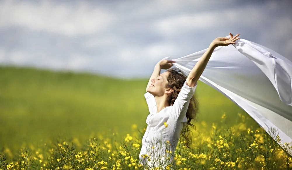 Woman enjoying fresh air in a yellow flower field, wearing white organic cotton clothing