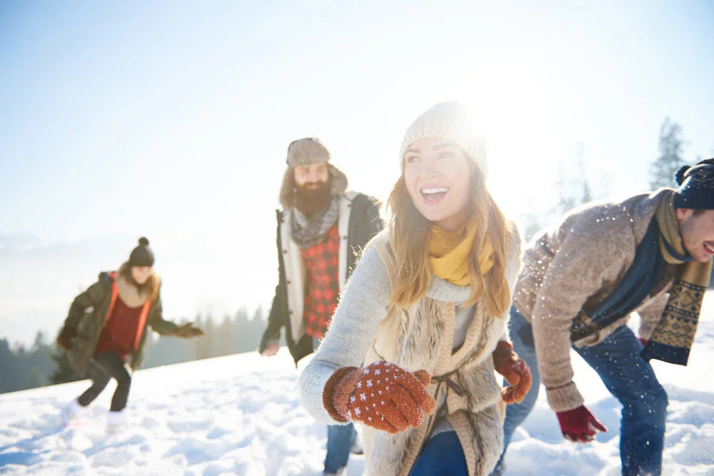 Group of adults wearing winter clothing laughing and playing in snowy outdoor setting