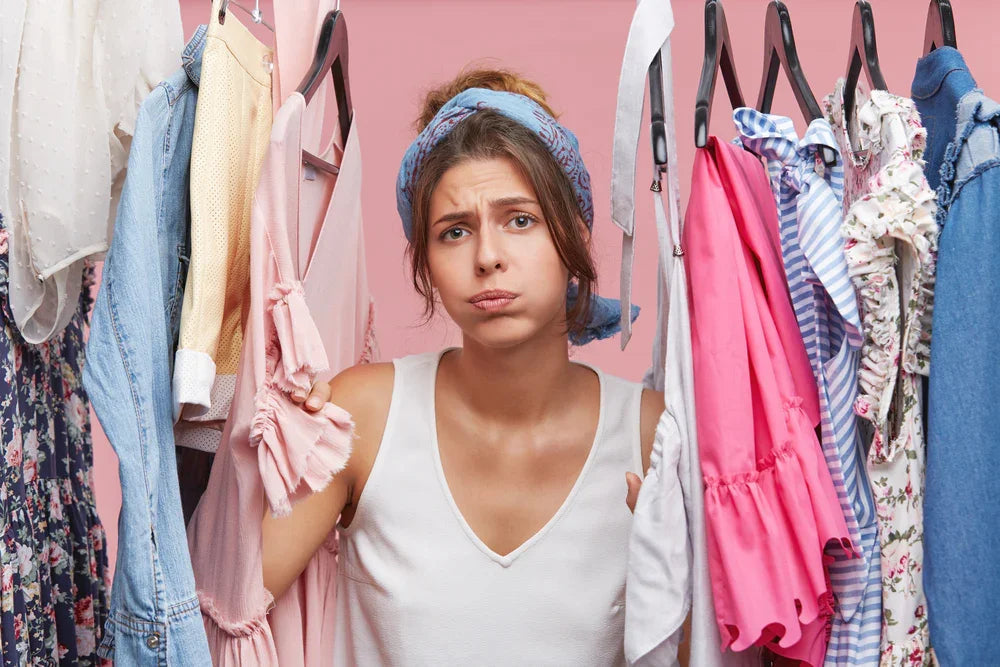 Woman with sensitive skin looking frustrated among cotton clothing on hangers