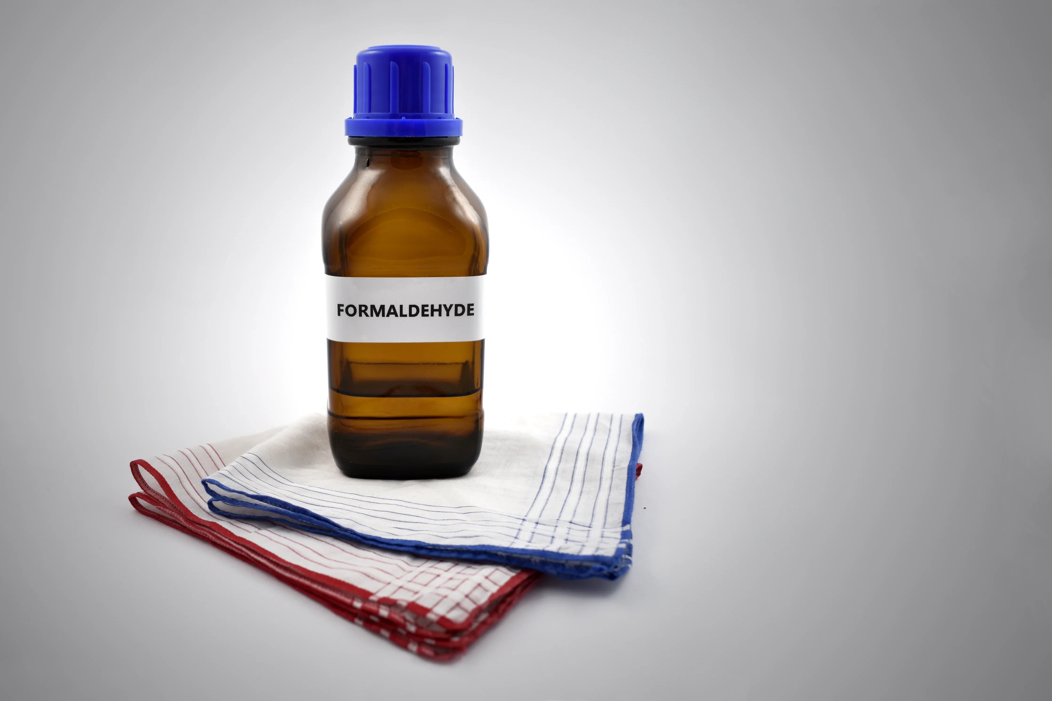 Brown formaldehyde bottle with blue cap on folded cotton handkerchiefs, highlighting allergen risk in clothing