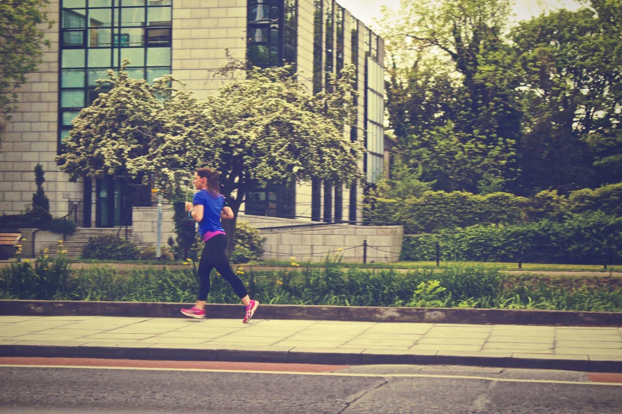 Woman jogging outdoors on city sidewalk in activewear, greenery and modern building background
