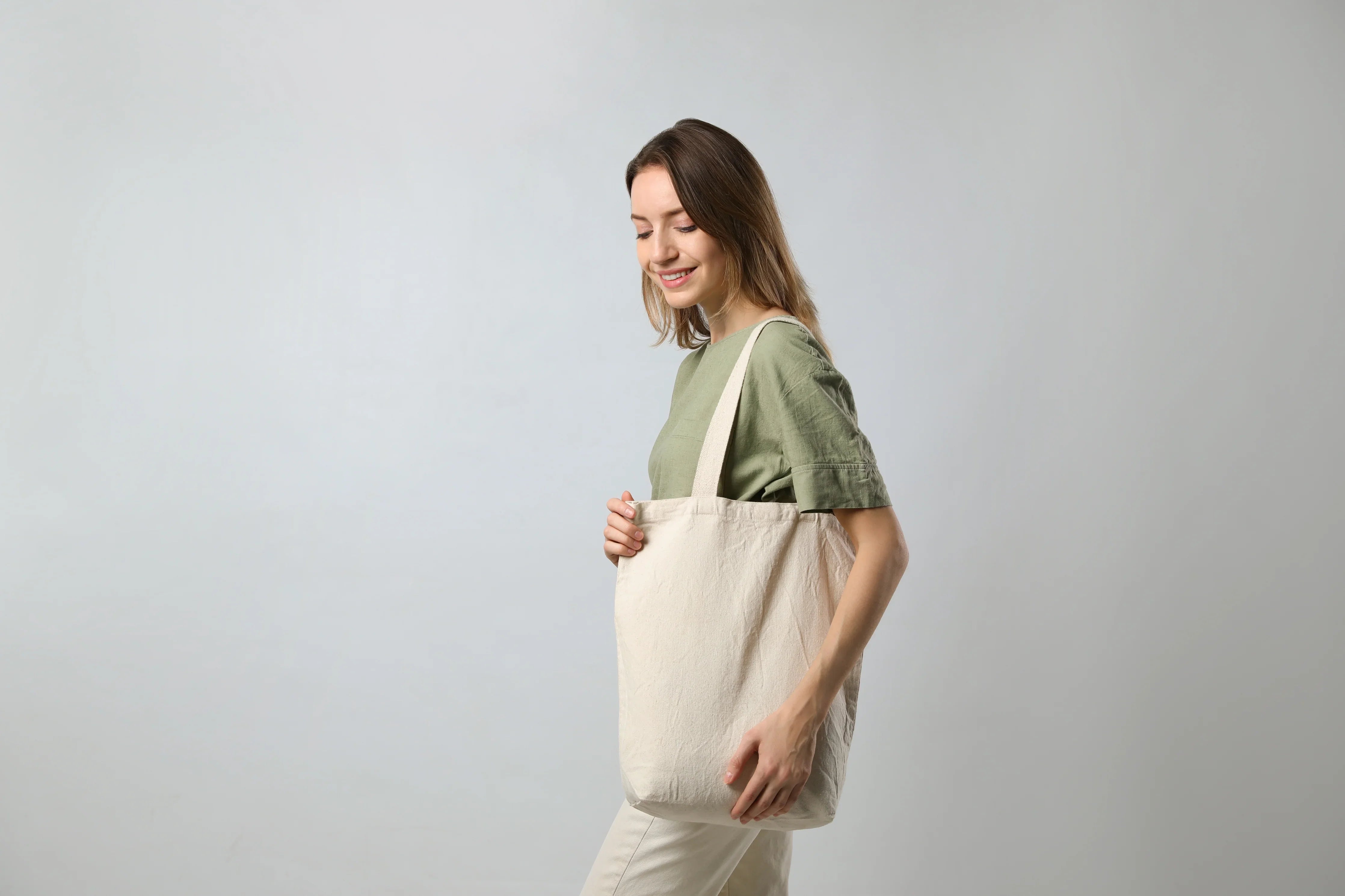 Woman with beige organic cotton tote bag and green shirt, minimal background