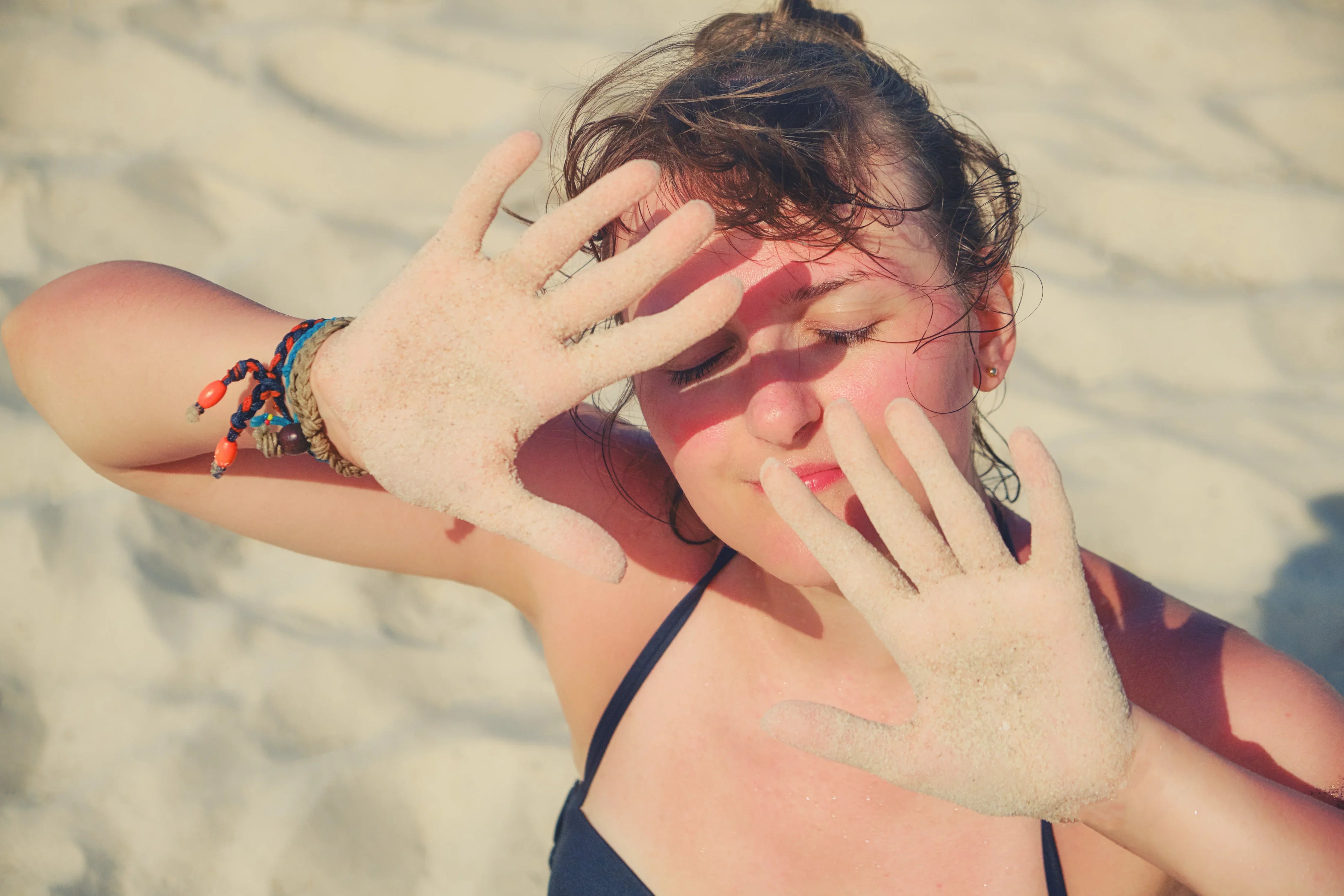Woman on sandy beach shielding face from sun, wearing allergy-free apparel, Cottonique