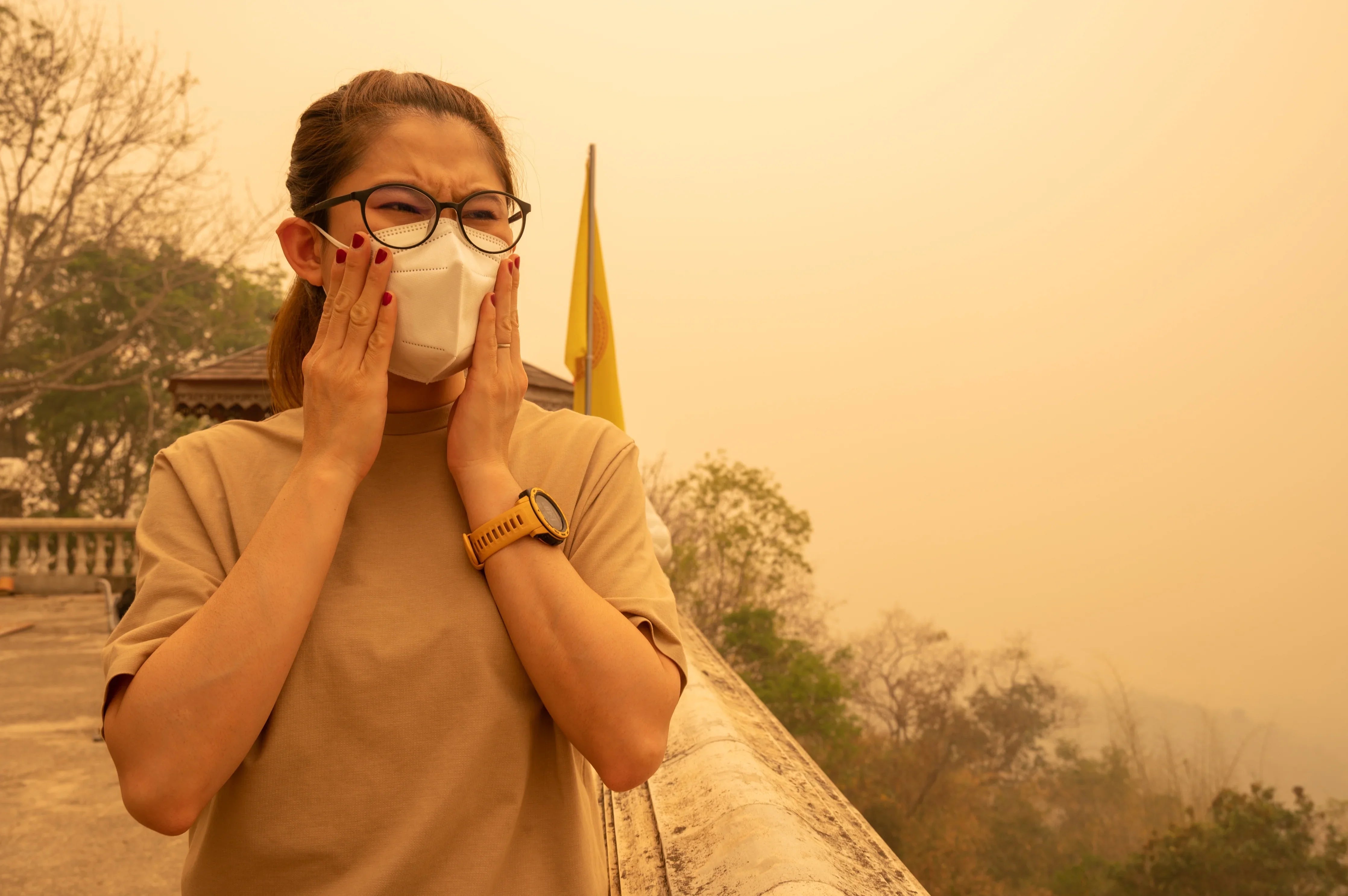 Woman wearing cotton shirt and mask outdoors in smoky air, showing allergy discomfort