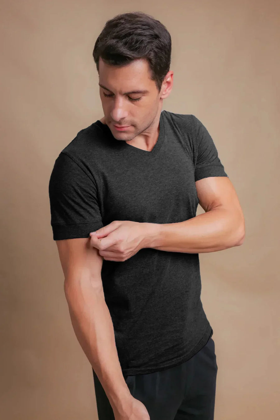 Man wearing black organic cotton V-neck T-shirt, rolling up sleeve for sensitive skin